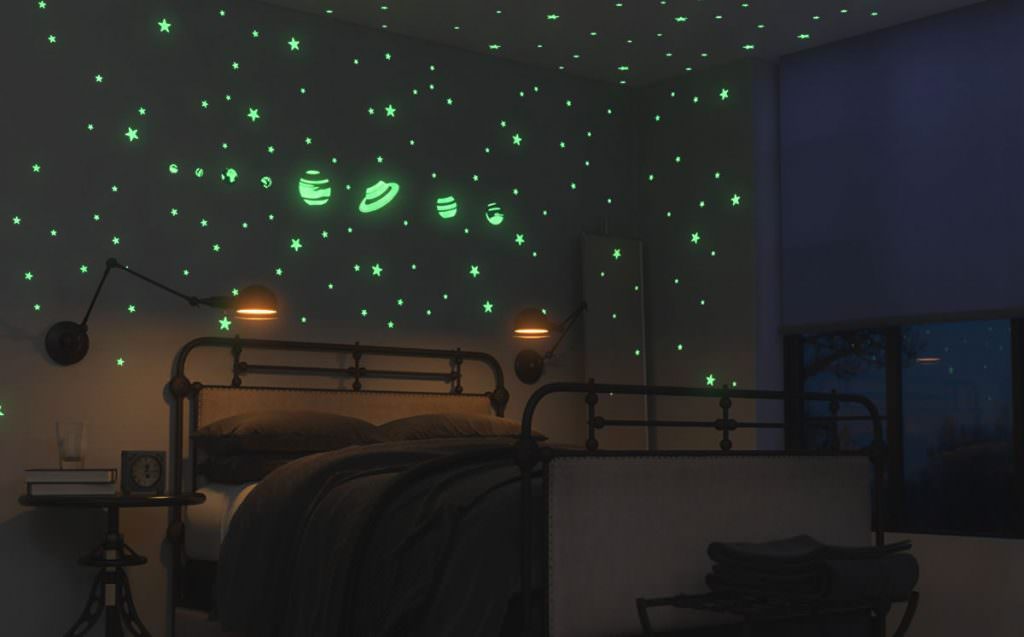 اتاق خواب پسر بچه ای که دیوارهای آن با استیکرهای شب تاب منظومه شمسی و ستاره ها دیزاین شده است